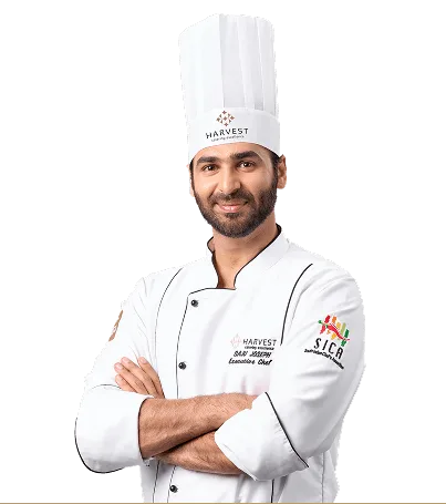 Professional chef in white uniform and hat posing confidently at Harvest Caterers.