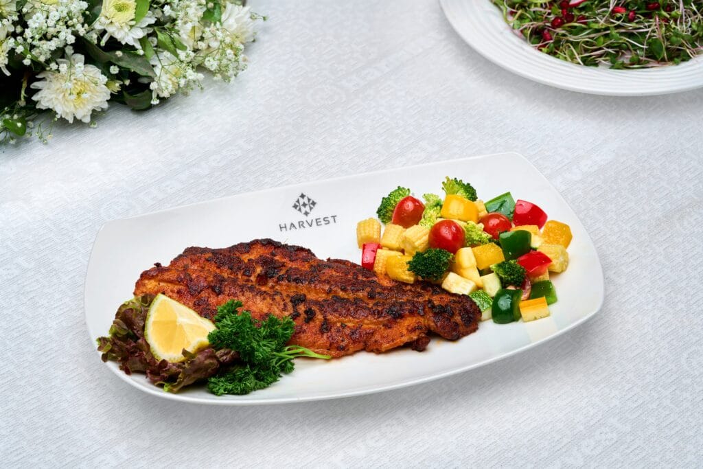 Harvest Caterers Kochi presenting pan-fried fish with lemon and vegetable sides.