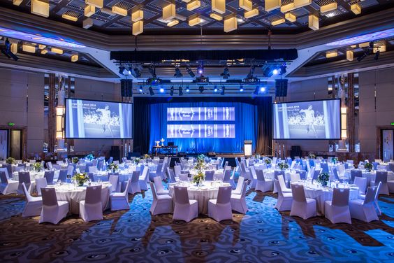 A grand corporate banquet hall setup with round dining tables, stage lighting, and formal seating, showcasing premium corporate event catering ideas.