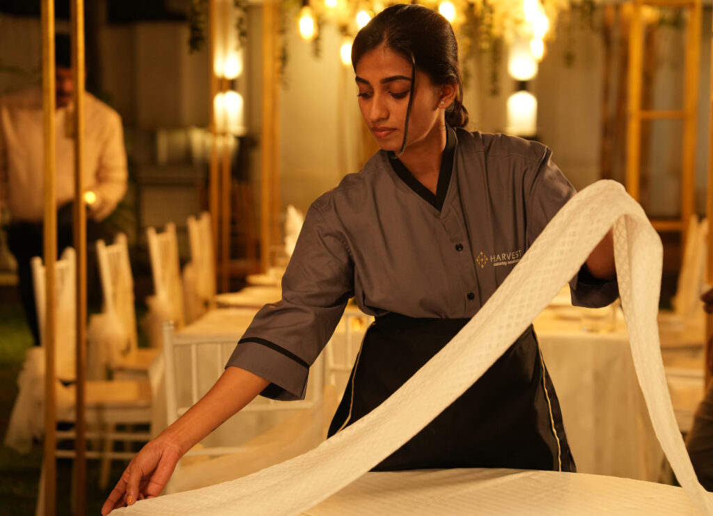Event staff member setting up a dining table with precision as part of professional wedding catering in Kochi.