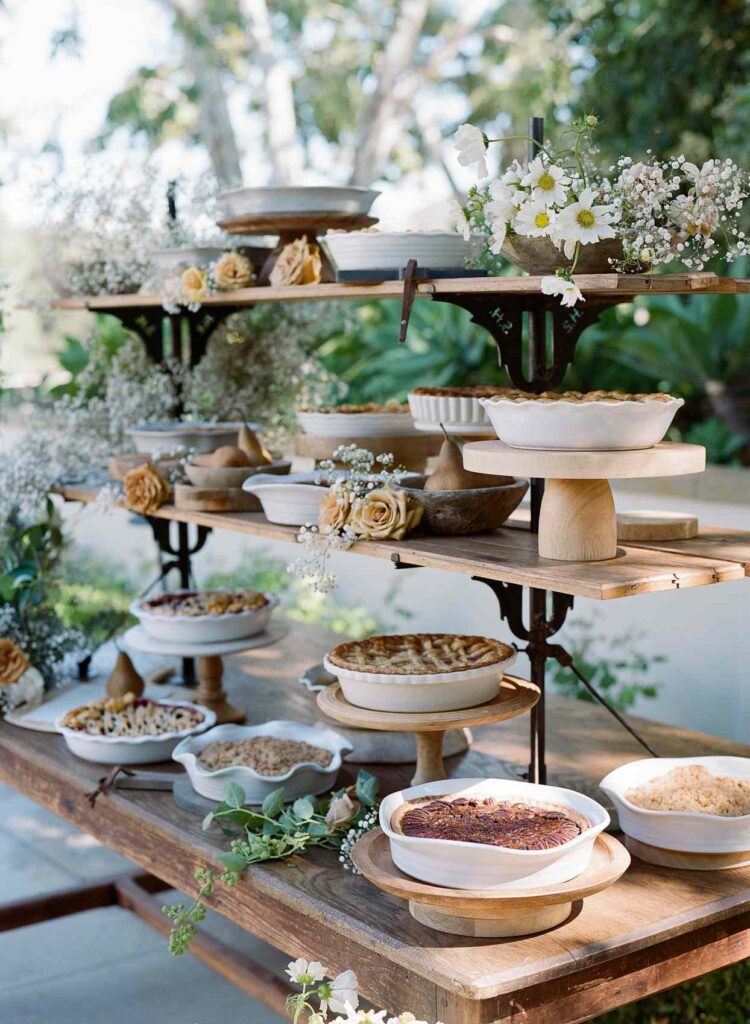 A beautifully styled rustic dessert table with handcrafted pies, wooden stands, and floral accents, showcasing the latest wedding catering trends in modern celebrations.